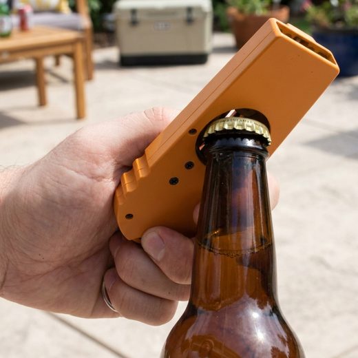 Orange plastic cap launcher device attached to a brown glass bottle held in a hand.