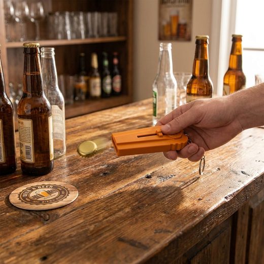Compact orange plastic cap launcher bottle opener held in a person's hand on a wooden surface.