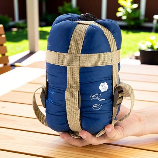 Blue ultra-portable sleeping bag compressed and secured with tan webbing straps on a wooden surface