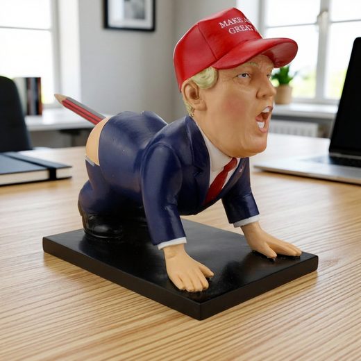 Donald Trump Pen Holder. Satirical resin figurine of a man in a red cap and blue suit posed on a black desk base.
