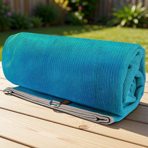 Turquoise woven camping mat rolled up and secured by a gray strap on a wooden outdoor table